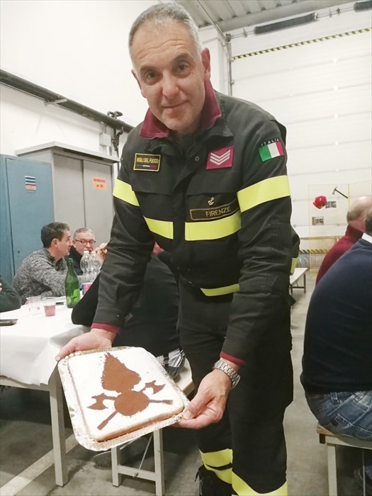 Un Vigile  presenta una torta con il logo del Corpo dei Vigili del Fuoco
