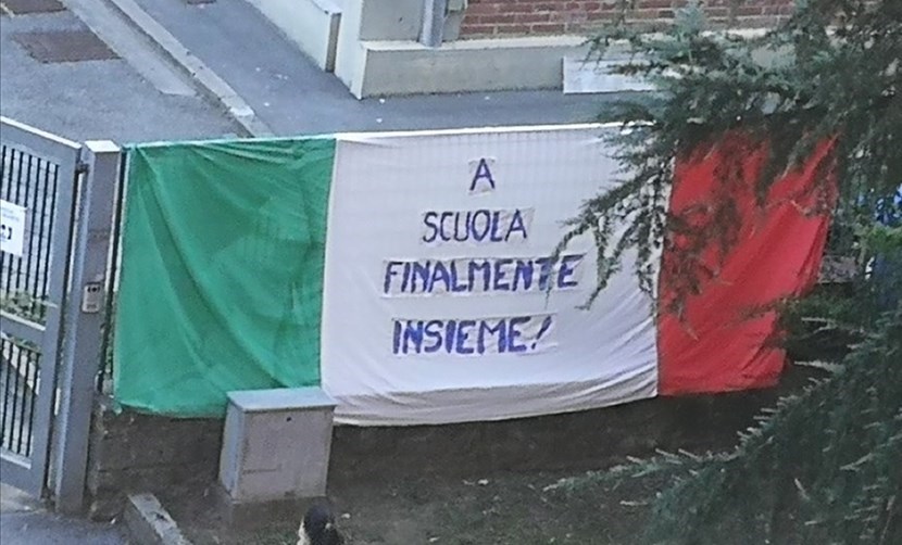 'A scuola - Finalmente insieme'. La scritta sulla bandiera italiana accoglie i bambini a Borgo