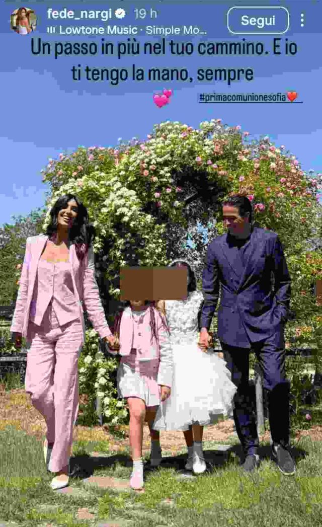 Federica Nargi in tailleur rosa pastello e Alessandro Matri in completo blu scuro sorridono con le figlie Sofia e Beatrice, circondati da fiori bianchi e rosa, durante la prima comunione di Sofia.