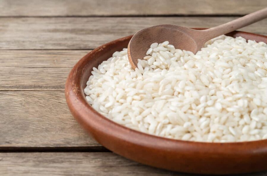 Riso bianco in una ciotola di legno, con cucchiaio di legno e poggiato su una tavola