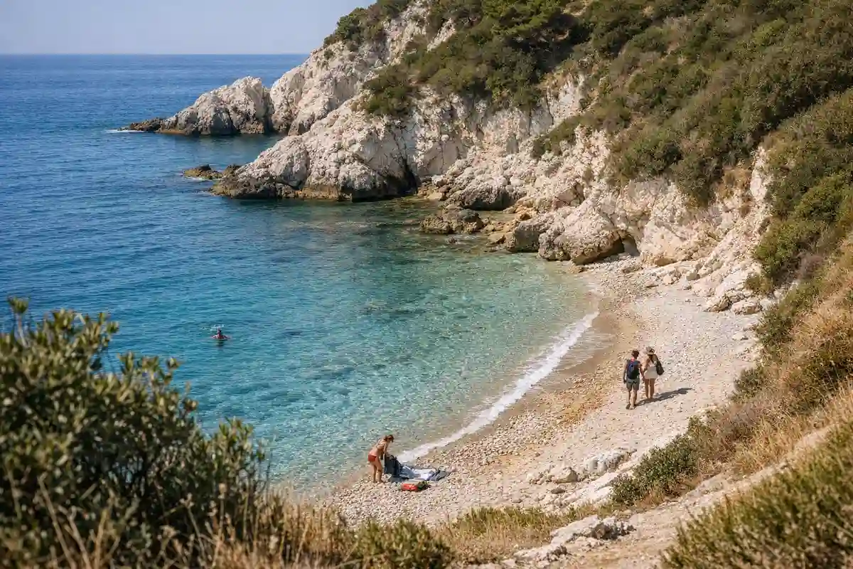 Caletta mediterranea con acqua turchese, spiaggia di ciottoli e falesie chiare, con pochi bagnanti