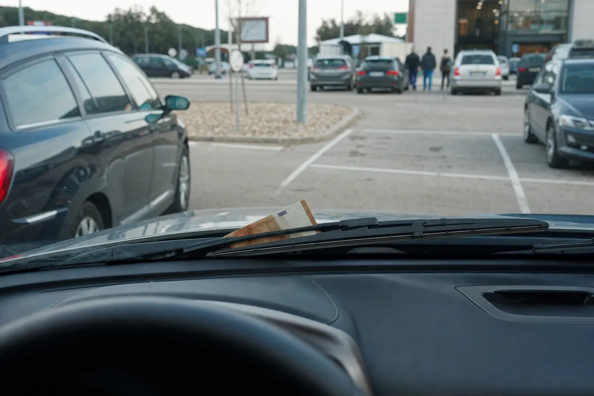 Banconota infilata sotto il tergicristallo vista dall’interno di un’auto parcheggiata in un parcheggio di area di servizio