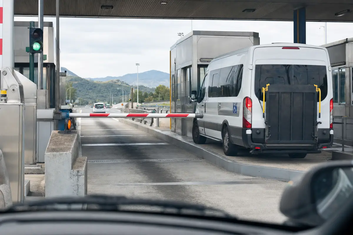 Casello autostradale con sbarra e furgone bianco con pedana e simbolo disabili nella corsia accanto