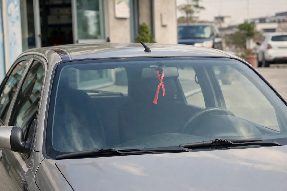 Nastro rosso legato allo specchietto retrovisore interno visto attraverso il parabrezza di un’auto grigia