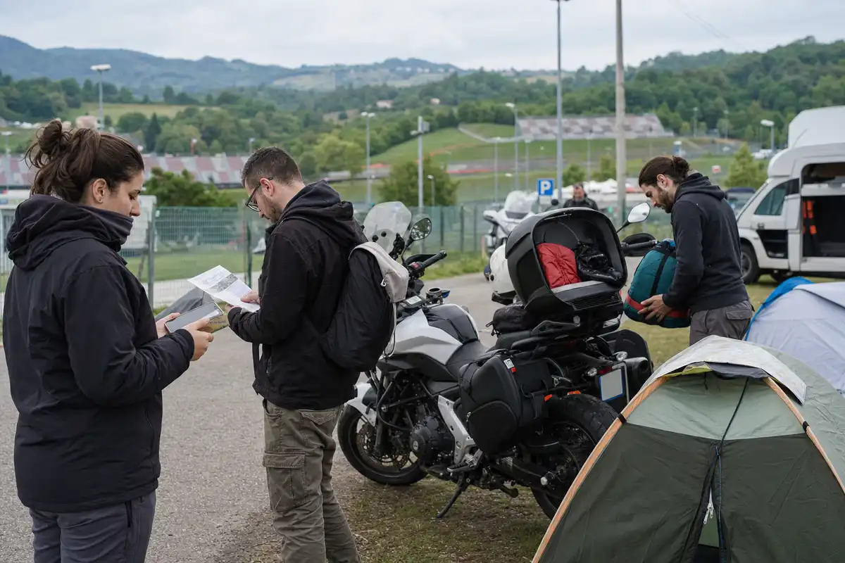 Tifosi in moto controllano biglietti e mappa accanto a tenda da campeggio vicino a un circuito tra le colline
