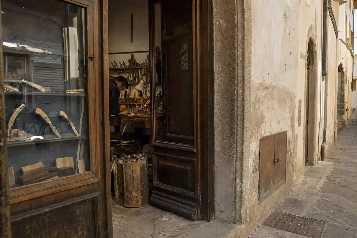 Ingresso di una bottega di coltelli con vetrina e artigiano al banco su una stretta via del centro storico