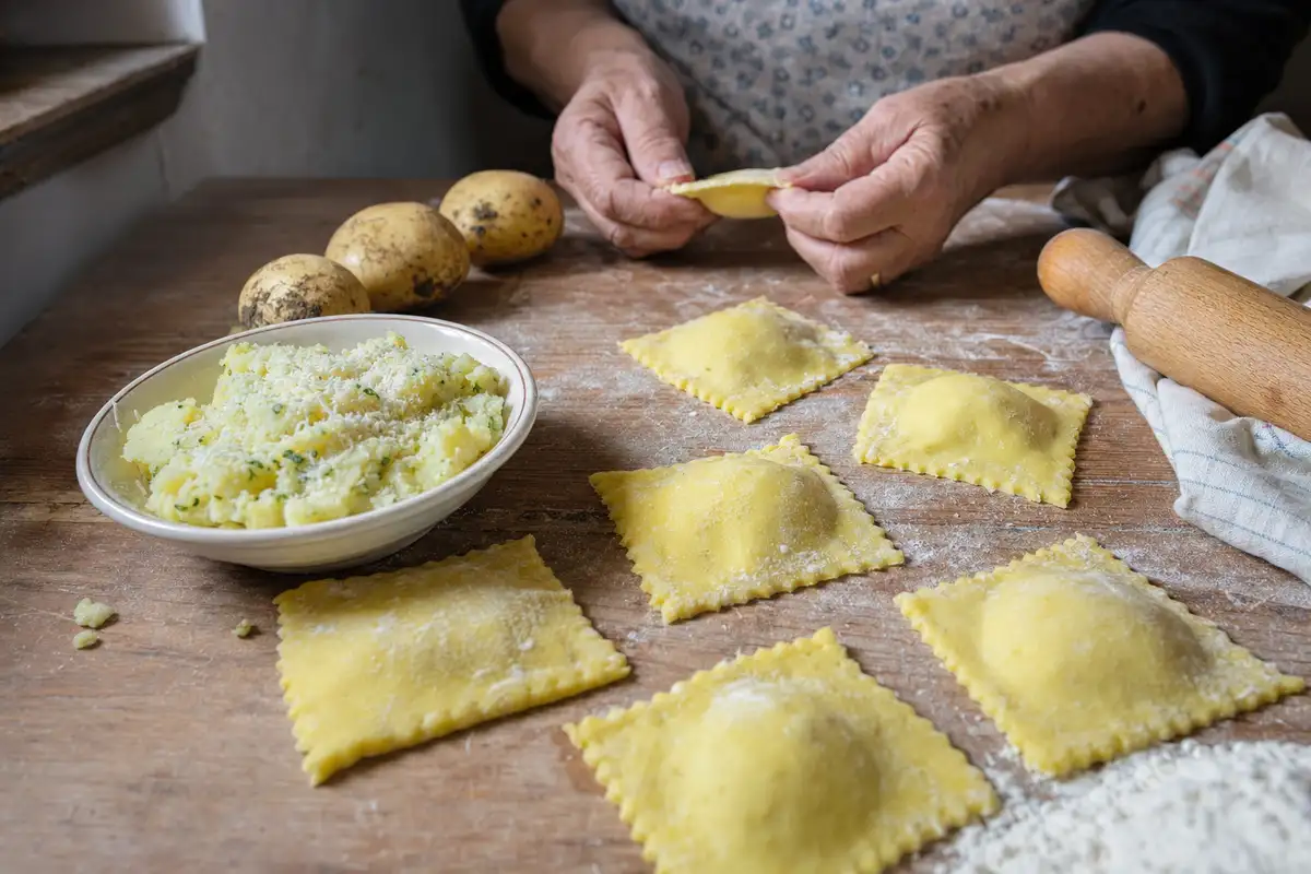 Tortelli di patate quadrati fatti a mano su tavolo infarinato, con ripieno in ciotola e mani che li chiudono