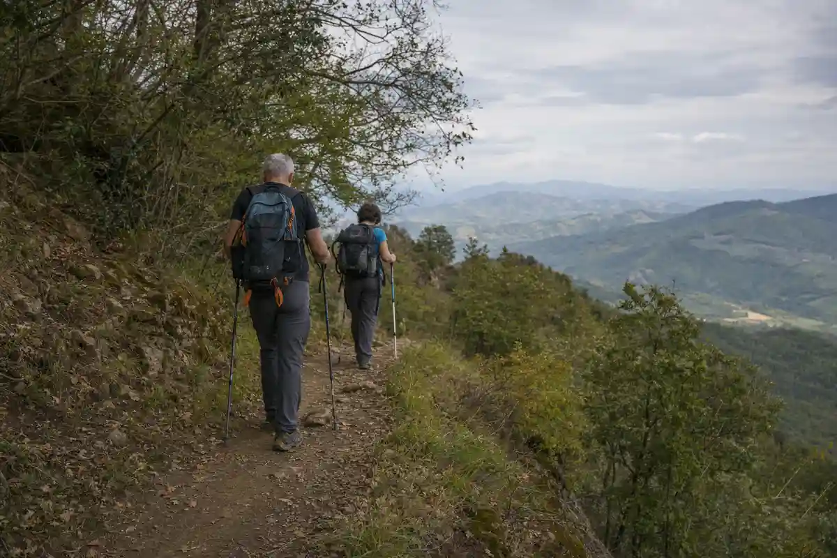 Due escursionisti di spalle con zaini e bastoncini su un sentiero di crinale, con vallate sullo sfondo