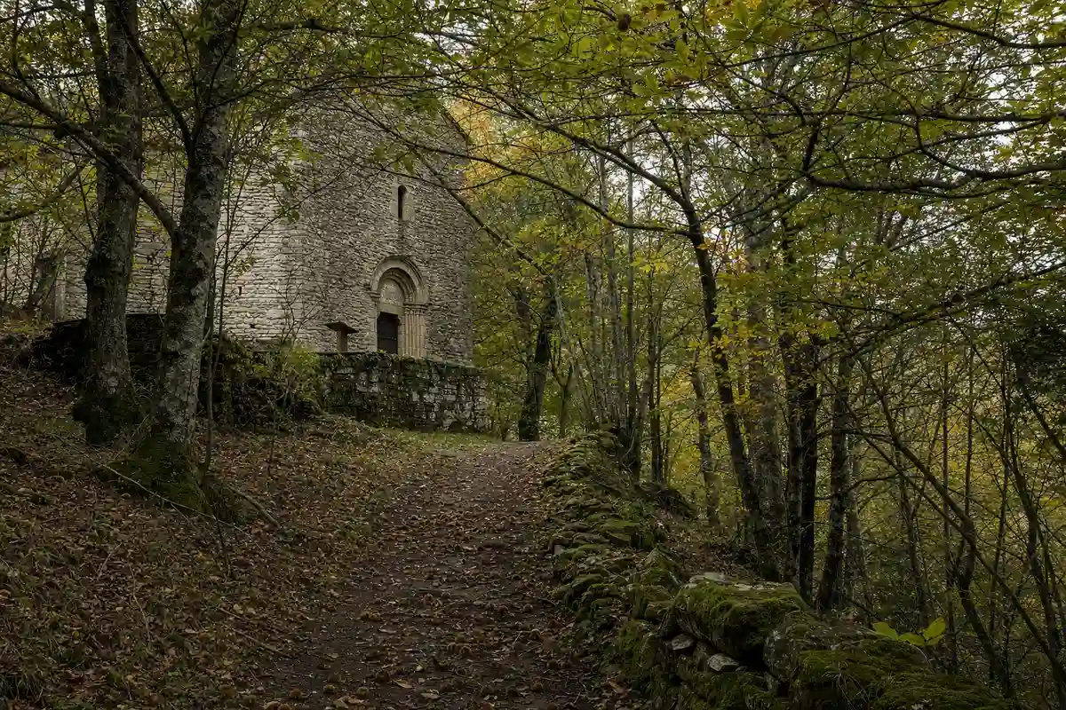Sentiero nel bosco con muro in pietra coperto di muschio e facciata di abbazia tra gli alberi