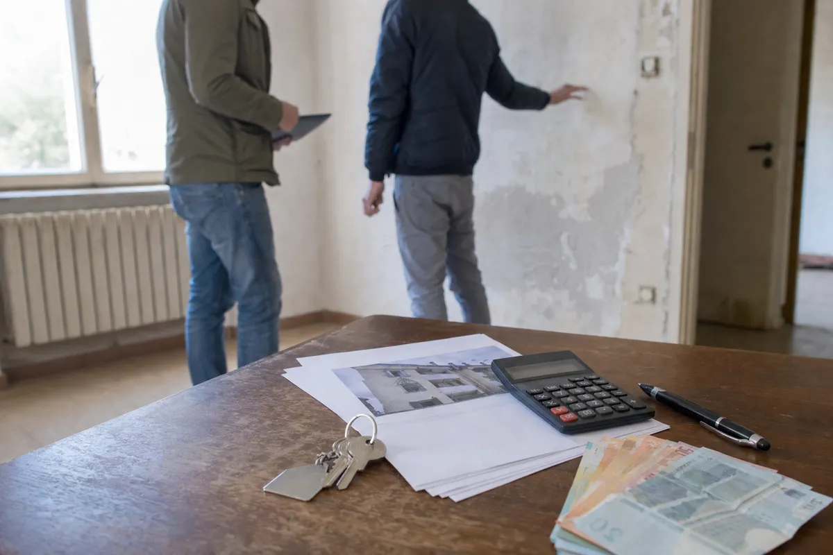 Chiavi di casa, documenti, calcolatrice e banconote su un tavolo durante l’ispezione di un appartamento
