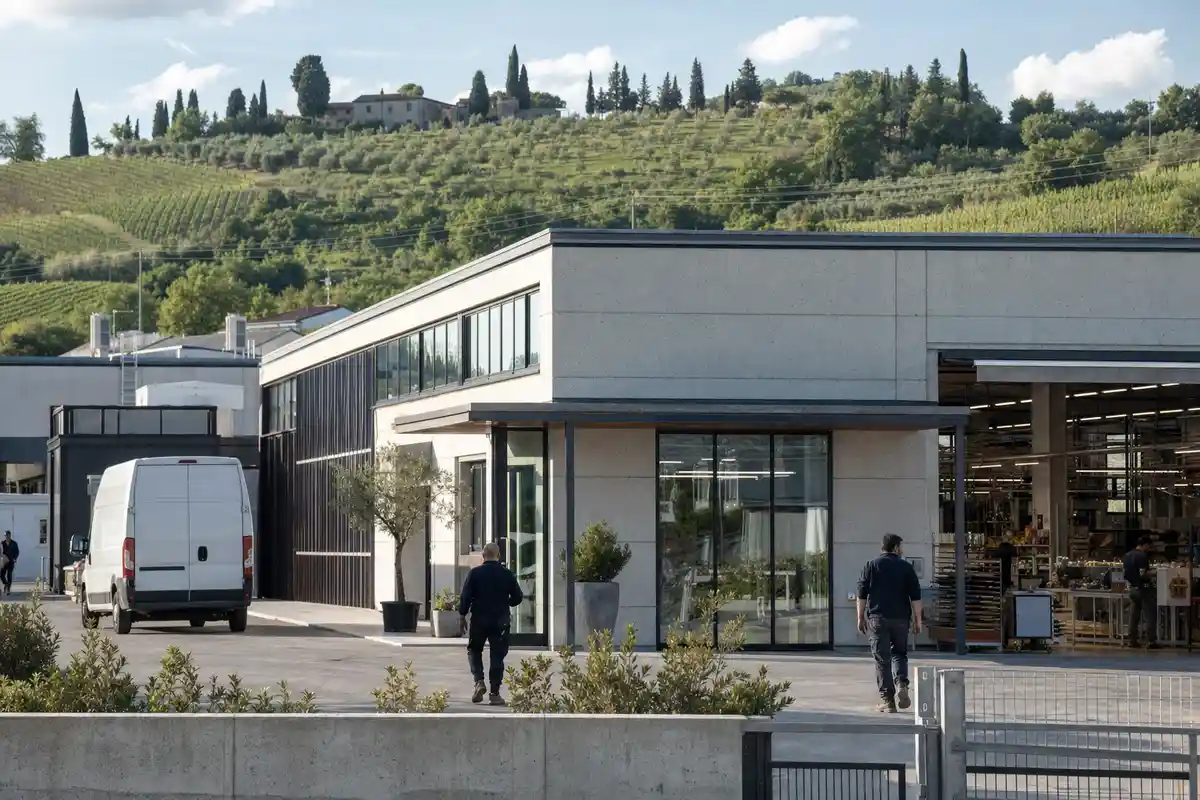 Stabilimento moderno con furgone e operai, sullo sfondo colline del Chianti con vigneti e cipressi