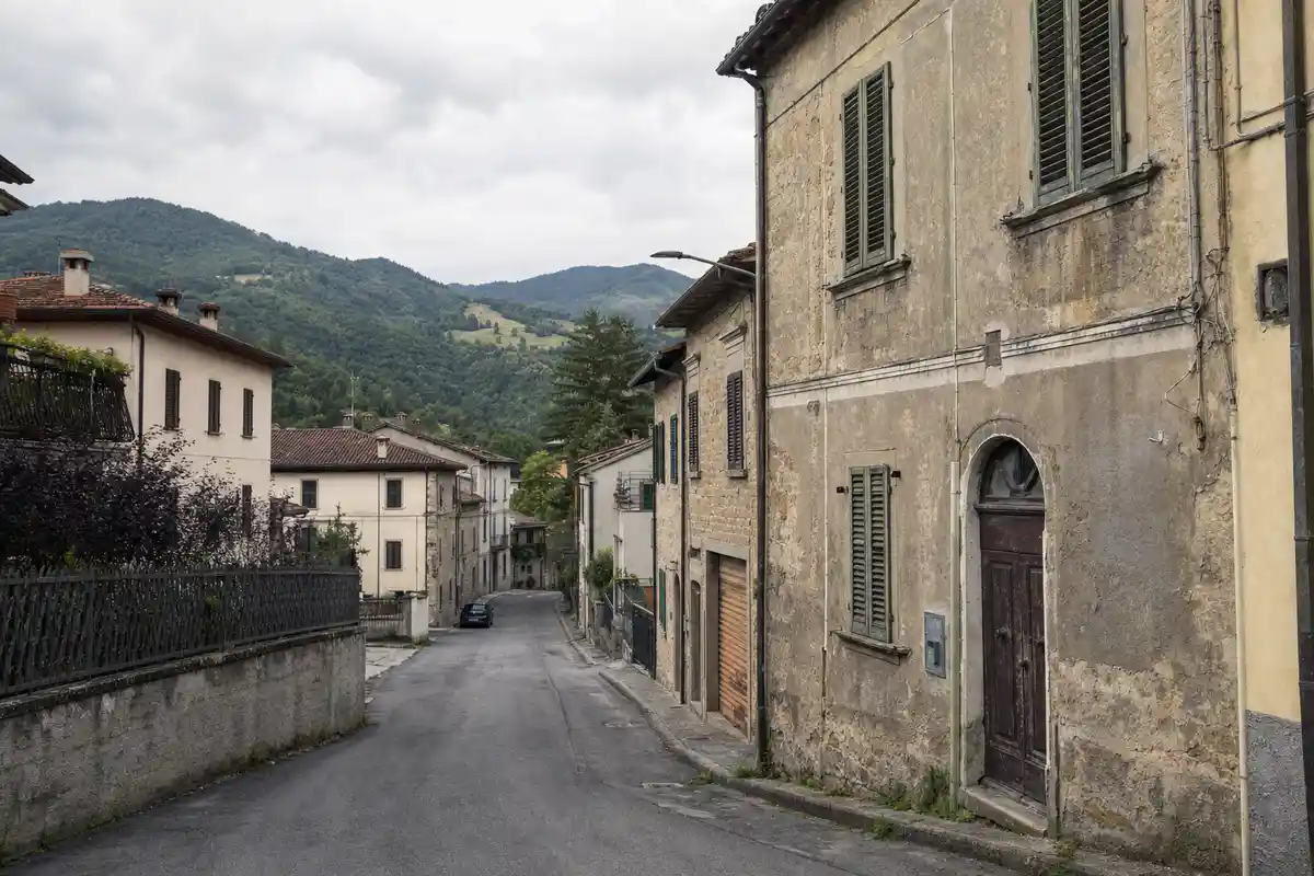 Strada tranquilla di borgo con case in pietra un po’ usurate e colline verdi sullo sfondo