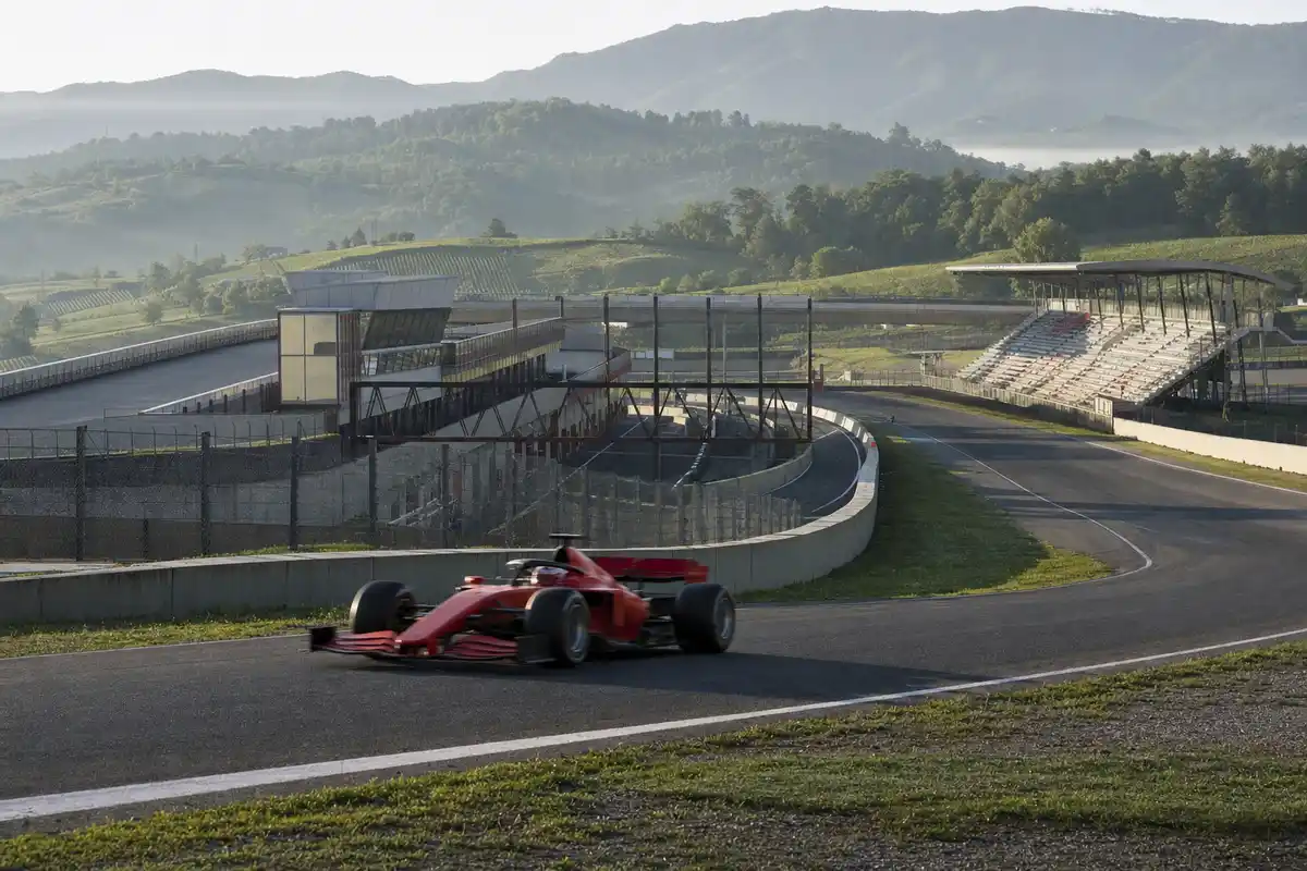 Monoposto rossa su un circuito con tribune vuote e colline verdi sullo sfondo