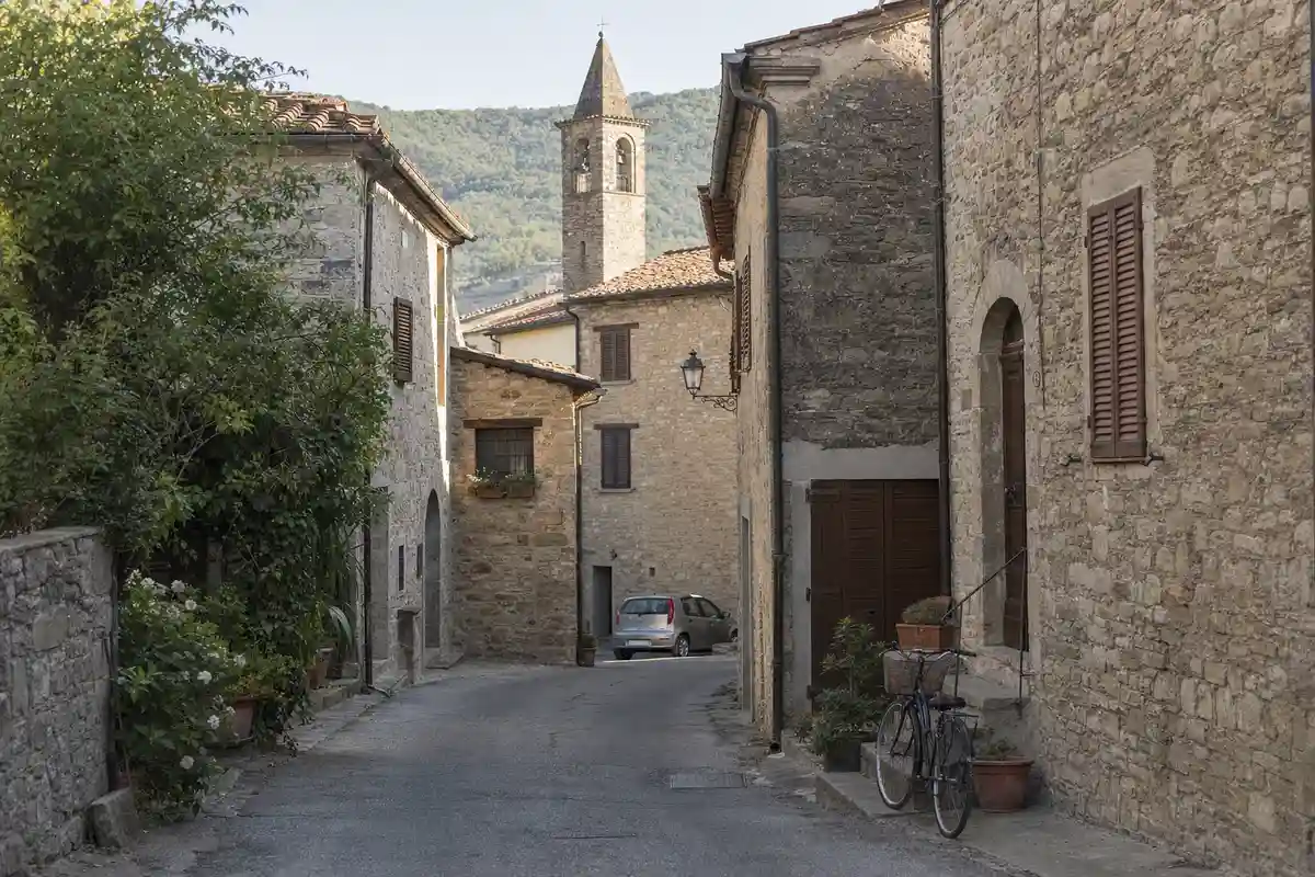 Strada stretta tra case in pietra con bicicletta appoggiata al muro e campanile in lontananza