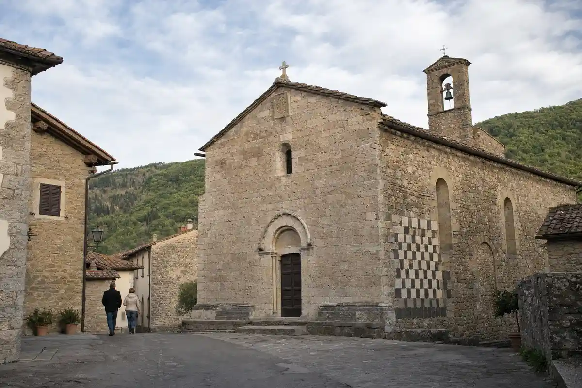 Facciata in pietra di una pieve romanica con decorazione a scacchiera e due persone che camminano nel borgo